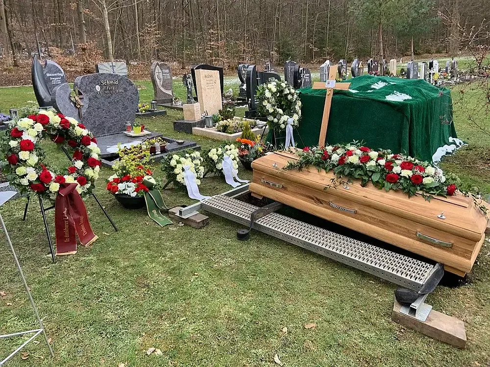 Sarg steht auf Grablegungsvorrichtung auf Rasenfläche, bereit für traditionelle Erdbestattung